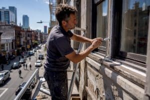 Hands applying fresh caulking on building window exterior