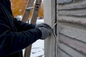 Hands removing cracked caulk from exterior joint